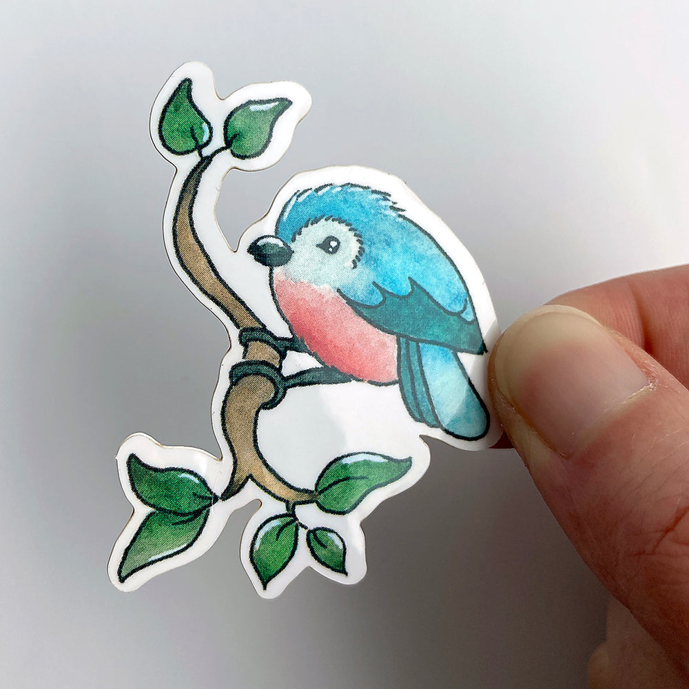 A vinyl sticker of an illustrated blue bird perched on a branch. This original watercolour and ink design is from the Found and Lost Art spring collection. 